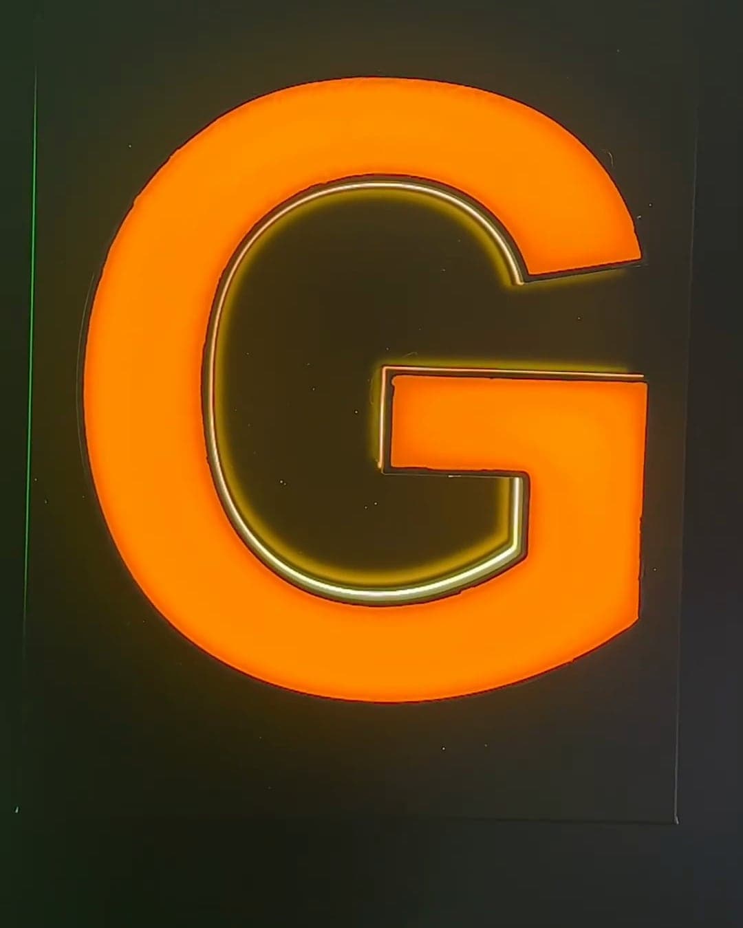 A letter G with a liquid-acrylic face, lit and glowing orange