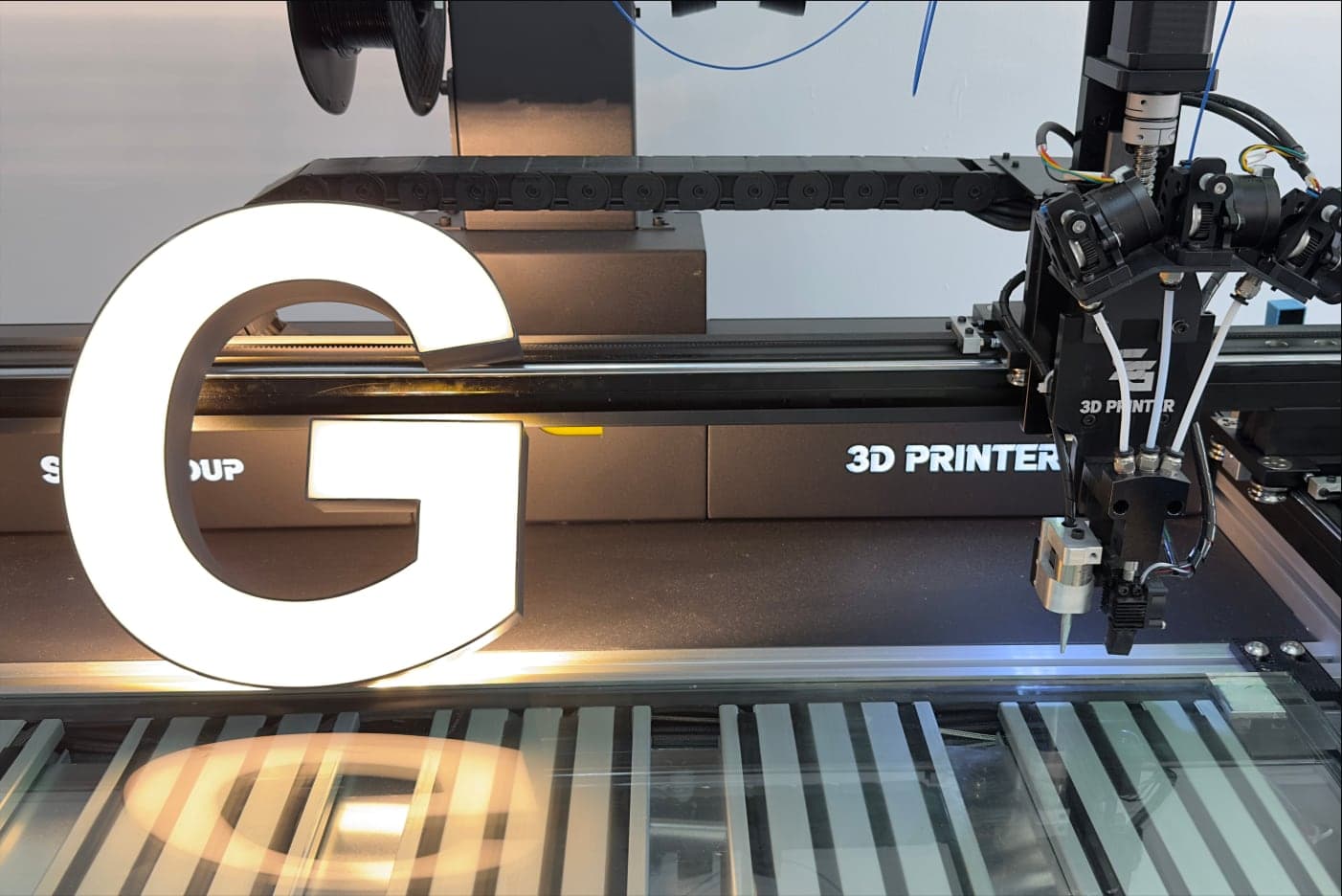 A finished letter G lit on an SG printer, with the Sign Group and 3D Printer plates behind it